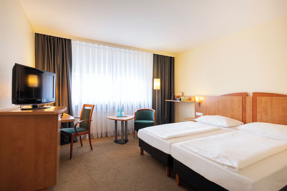 Une chambre d’hôtel avec deux lits, un bureau avec une télévision, une chaise, une petite table et une lampe.