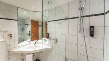 Un baño moderno con ducha de mampara de vidrio, un lavabo blanco y un espejo.