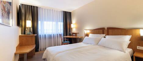 A hotel room with a double bed, bedside tables, a desk, a chair, and a window with curtains.