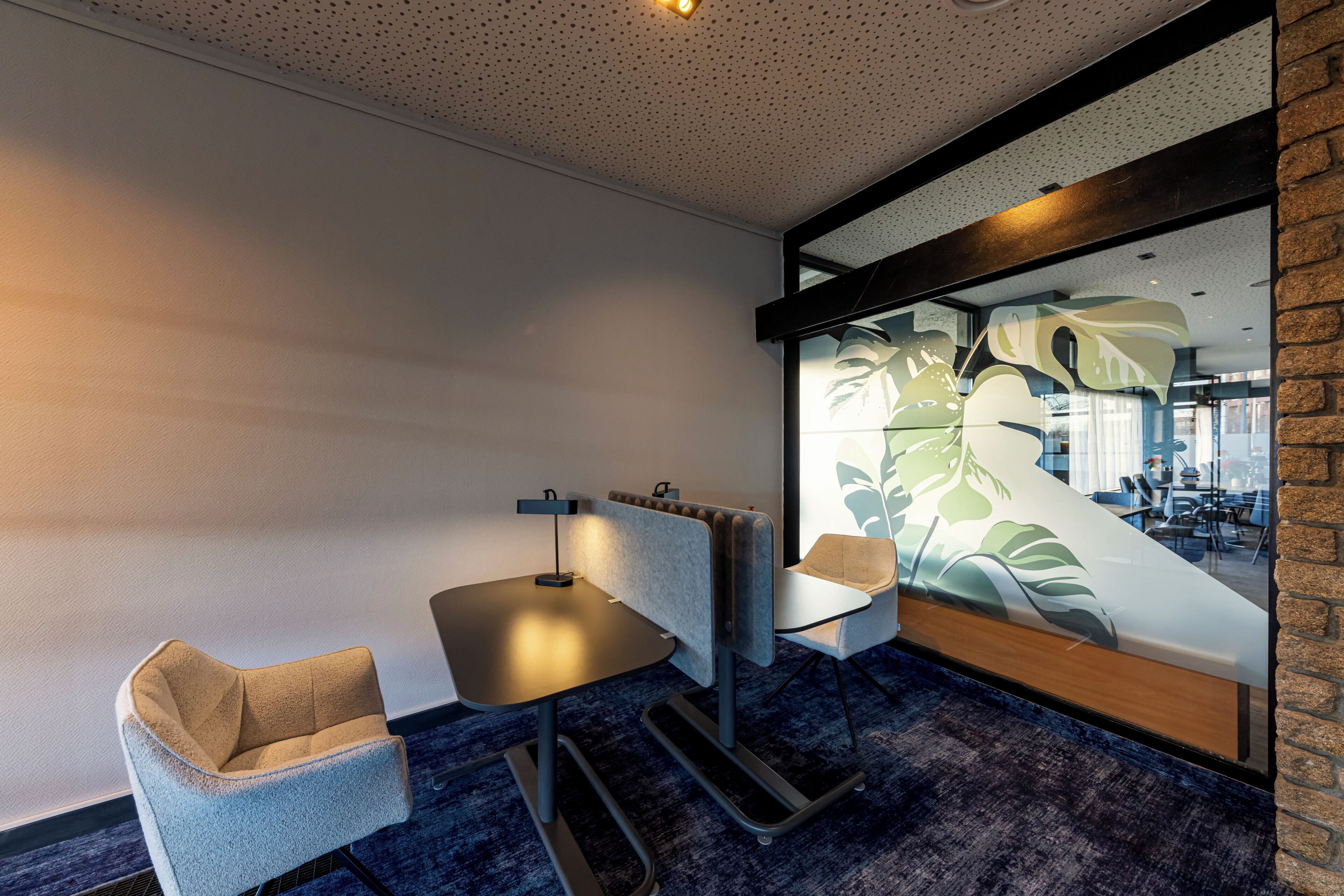 Ein modernes Zimmer mit Schreibtisch, zwei Stühlen, Heizkörper und großem Fenster mit Pflanzenmuster.