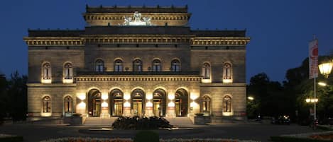 A large, historic building with a central statue, arched windows, and a well-lit entrance.