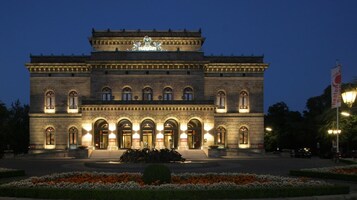 A large, historic building with a central statue, arched windows, and a well-lit entrance.