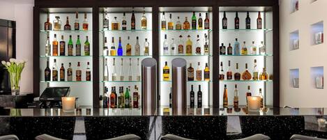 Un espace bar avec plusieurs étagères remplies de bouteilles d’alcool, une caisse enregistreuse et des tabourets de bar.