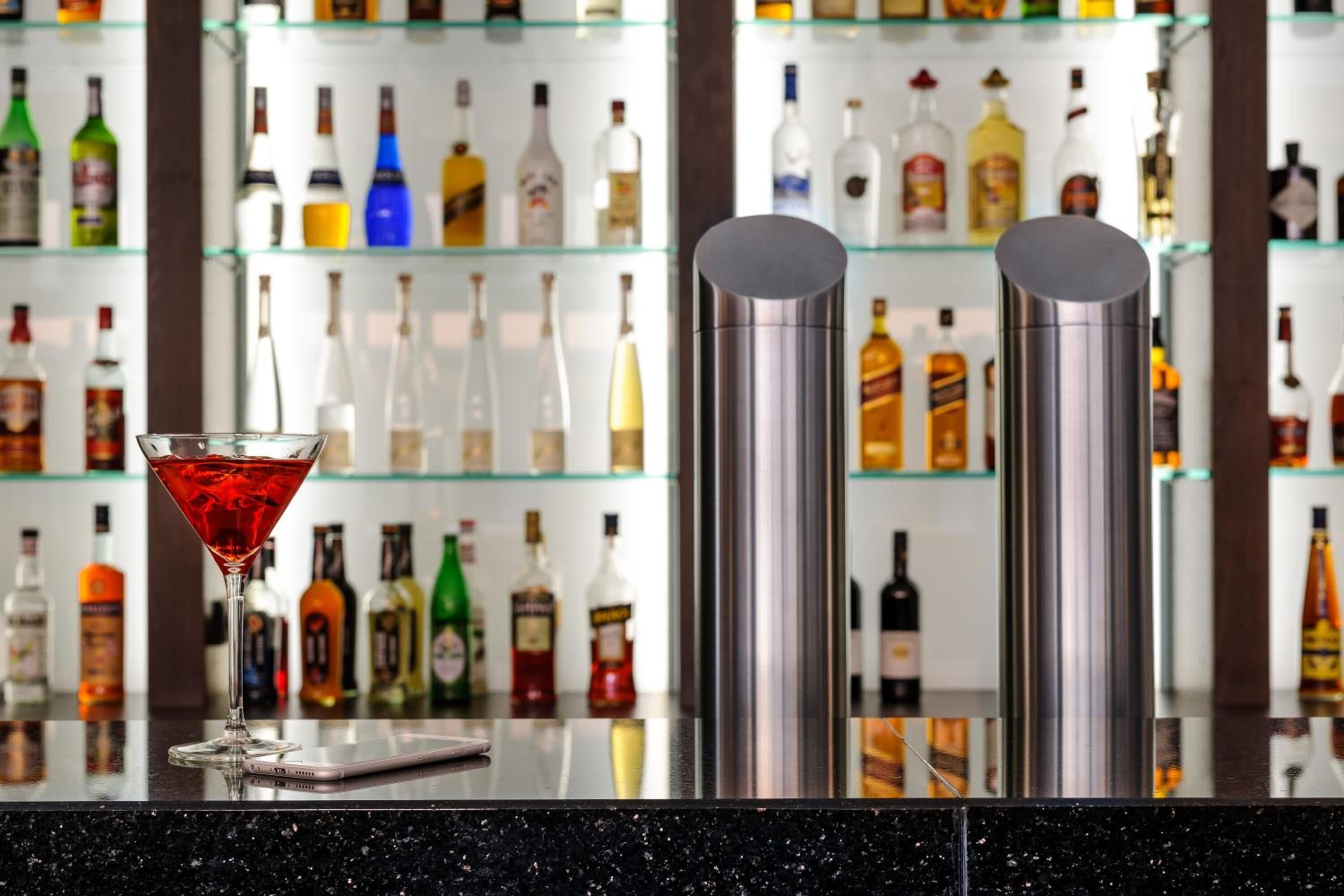 A bar area with a martini glass and two stainless steel shakers on a reflective countertop.