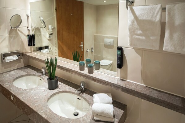 A modern bathroom with two sinks, a large mirror, and a shower area. - ACHAT Hotel Braunschweig (Braunschweig)