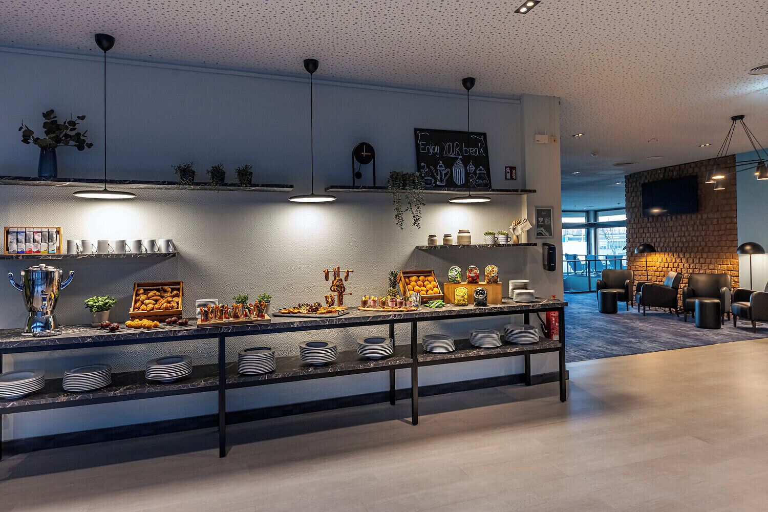 Un café moderne avec un comptoir en marbre, des étagères remplies de produits alimentaires et un espace salon avec des chaises.