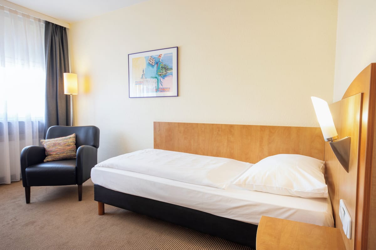 Une chambre d’hôtel avec un lit, une chaise, une lampe et un tableau au mur.