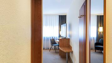 A hotel hallway with a carpeted floor, a wooden door, a desk with a chair, a computer, and a large mirror.