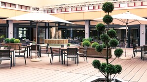 Une vaste terrasse extérieure dotée de nombreuses tables et chaises, entourée de plantes en pot et agrémentée de parasols.
