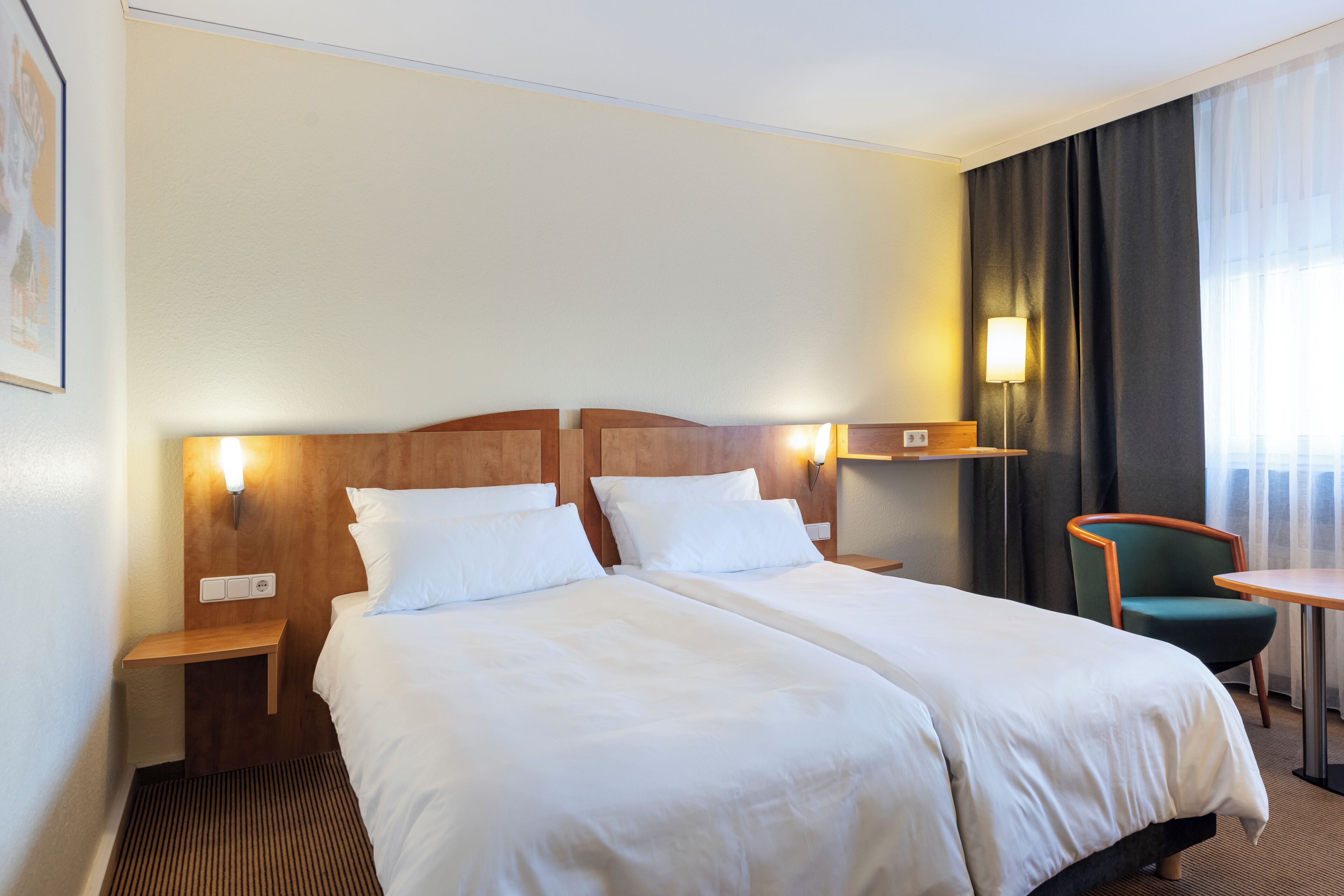 A hotel room with two beds, a desk, a chair, and a window with curtains.