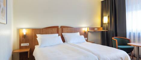 A hotel room with two beds, a desk, a chair, and a window with curtains.