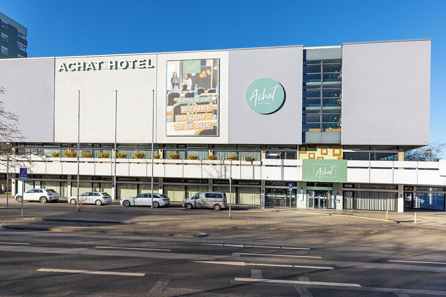 Un edifici d'hotel modern amb un cartell ben visible que diu 'Achat Hotel'.