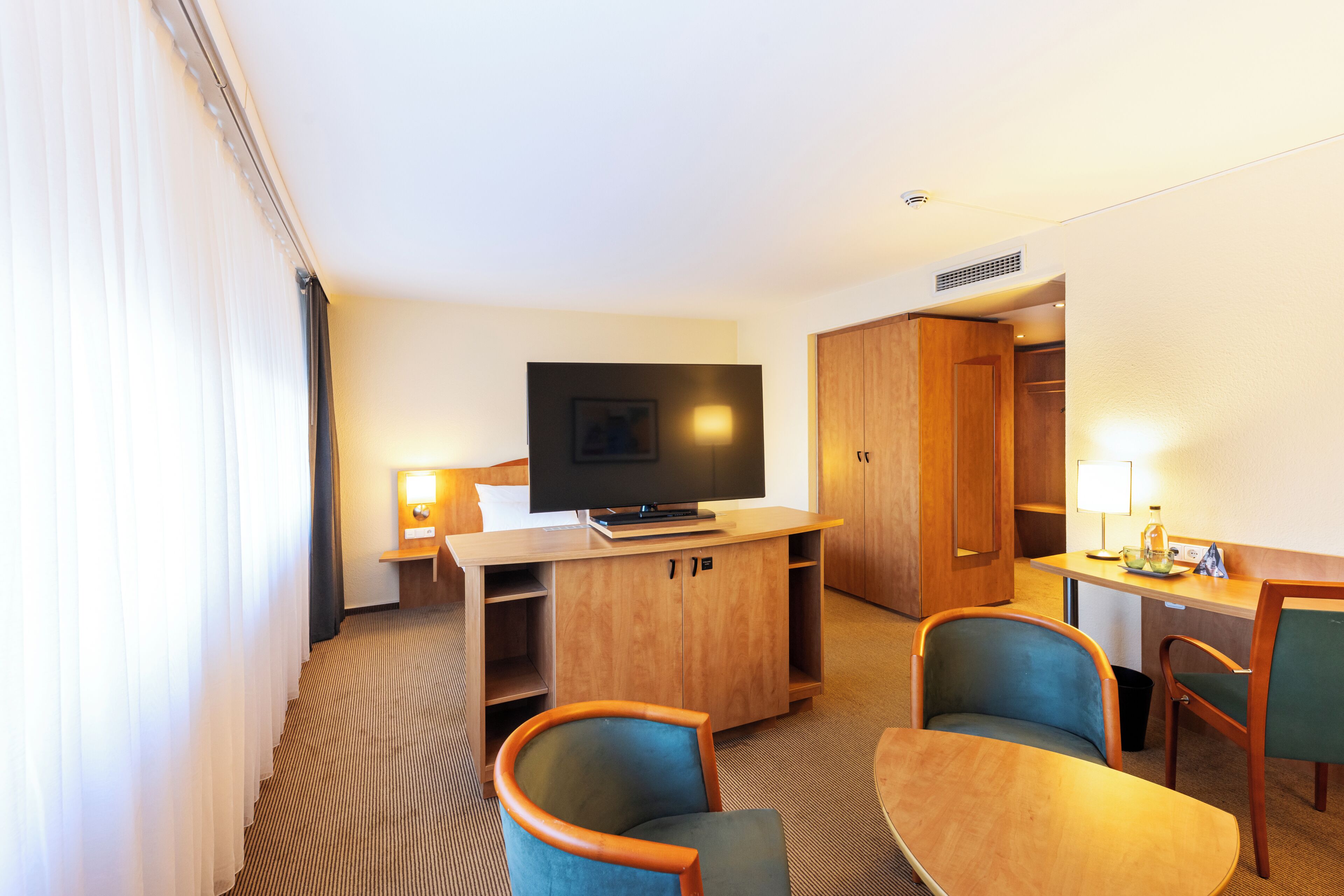 A hotel room with a television, a desk, a chair, and a bed.