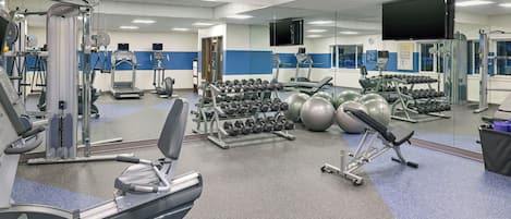 Ett gym med olika typer av träningsutrustning, inklusive löpband, hantlar och träningsbollar.