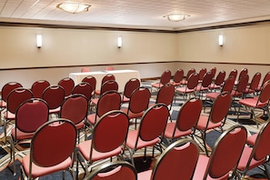 A conference room with rows of red chairs, a white table, and a patterned carpet.