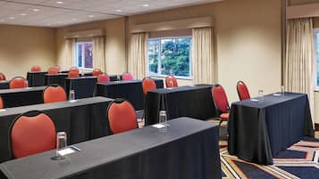 Un salón de conferencias con varias mesas y sillas, amplias ventanas con cortinas y piso alfombrado.