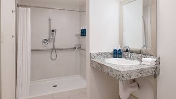 A modern bathroom with a shower, grab bar, sink, and mirror.