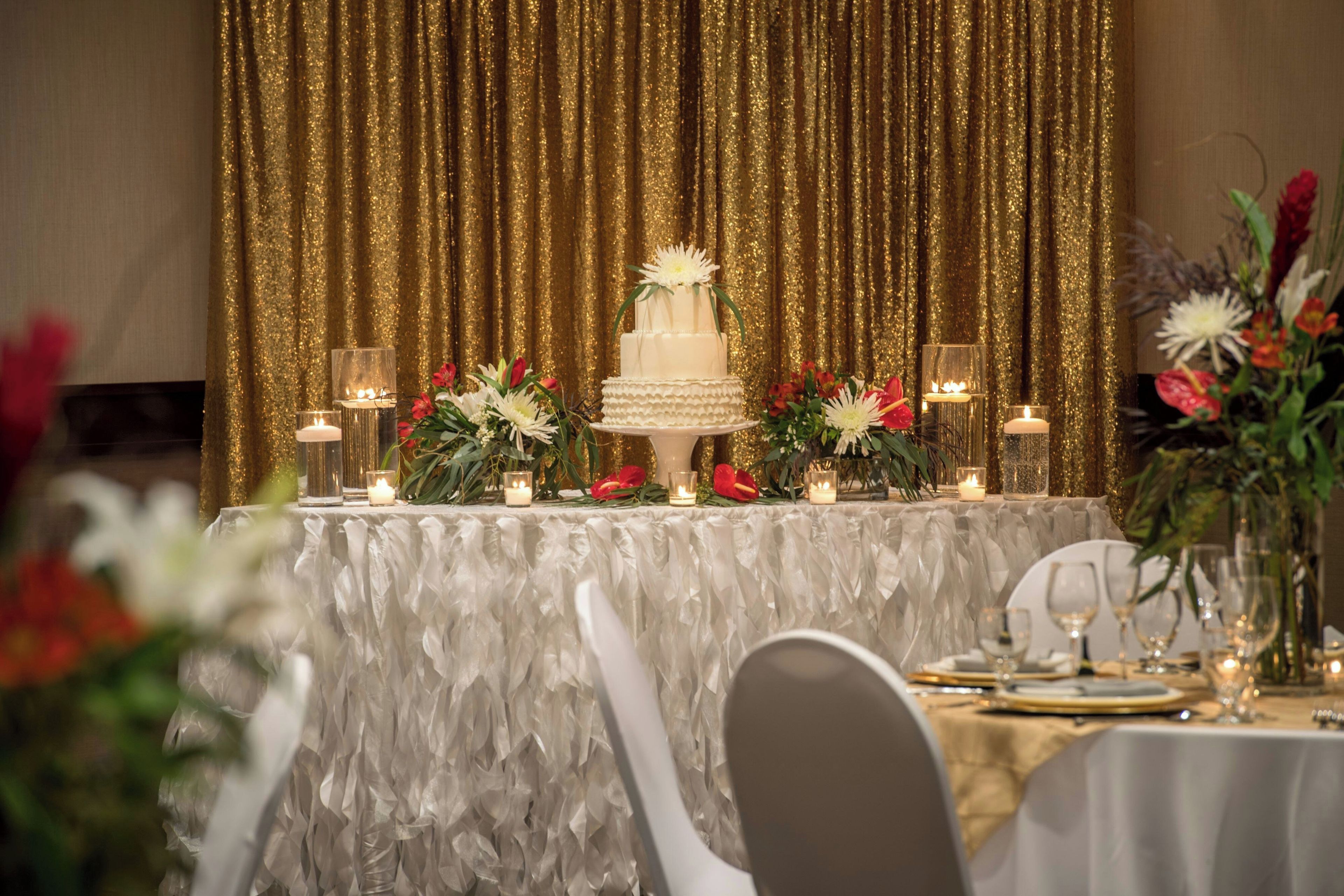 Una mesa de banquete con un pastel blanco de varios niveles, arreglos florales y velas.