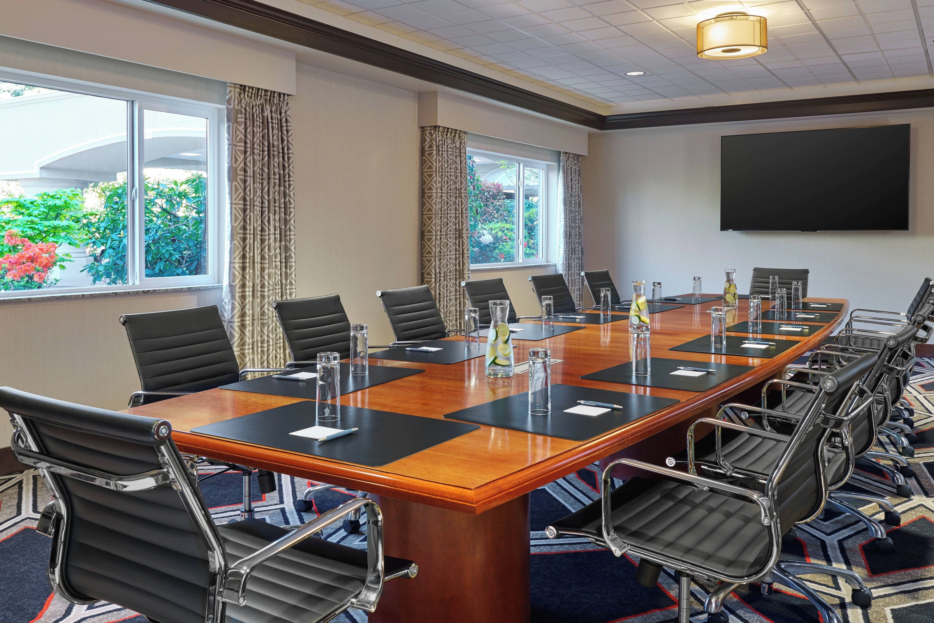 A conference room with a long table, black chairs, and a projector screen.