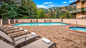 Un espace piscine doté de chaises longues et d’un jacuzzi, le tout entouré d’arbres et de montagnes.