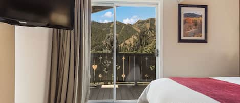 A hotel room with a bed, a television, a sliding glass door to a balcony, and a framed picture on the wall.