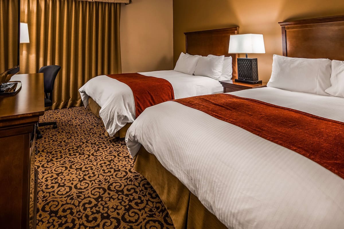 A hotel room with two beds, a desk, a chair, a lamp, and a patterned carpet.