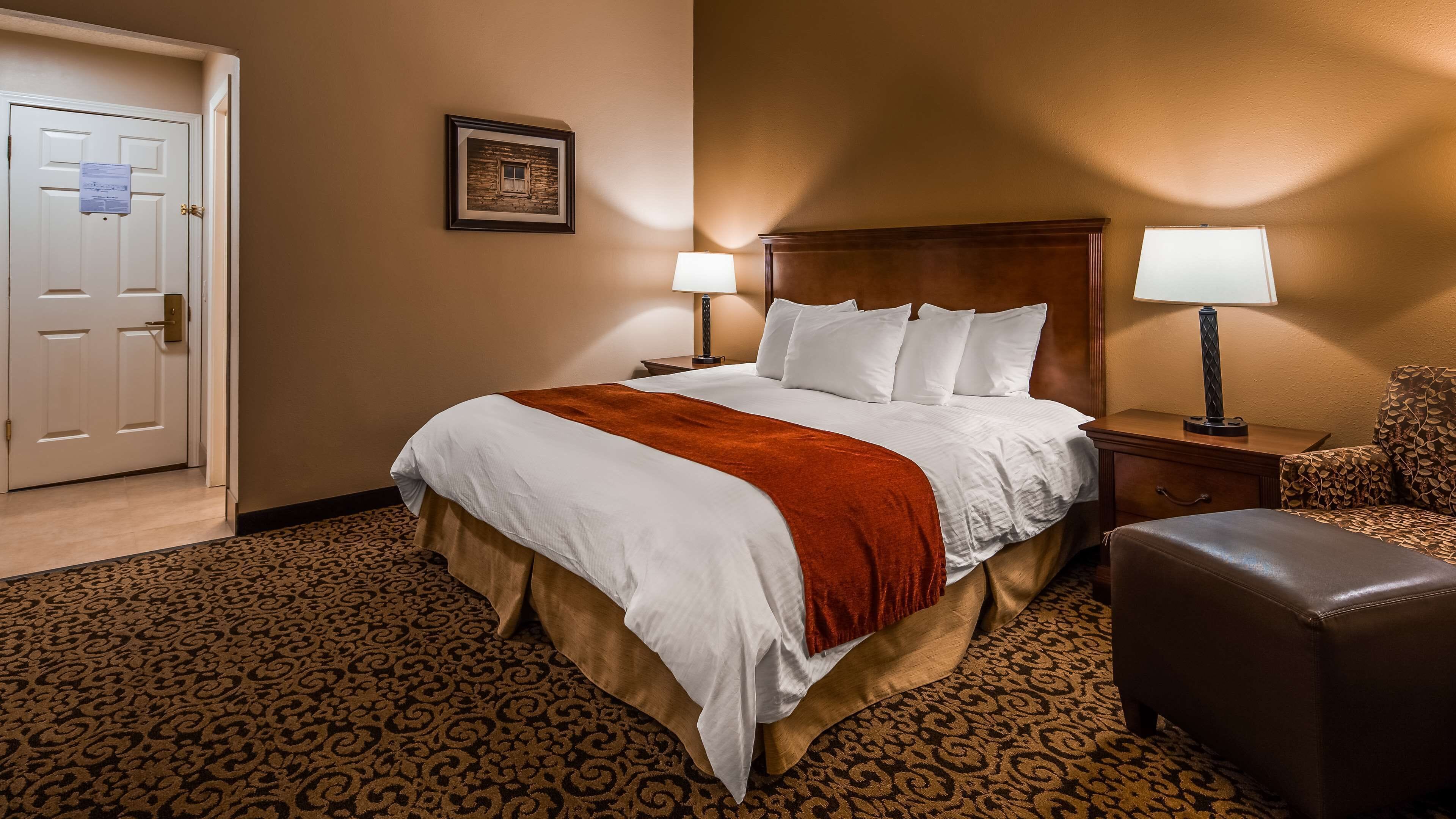 A hotel room with a large bed, two bedside tables with lamps, a patterned carpet, and a door with a notice.