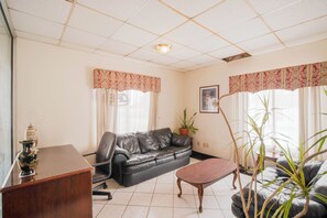 A living room with a leather sofa, a wooden coffee table, a desk, and a potted plant. - Hotel O Grand Inn Channelview I-10 (Channelview)