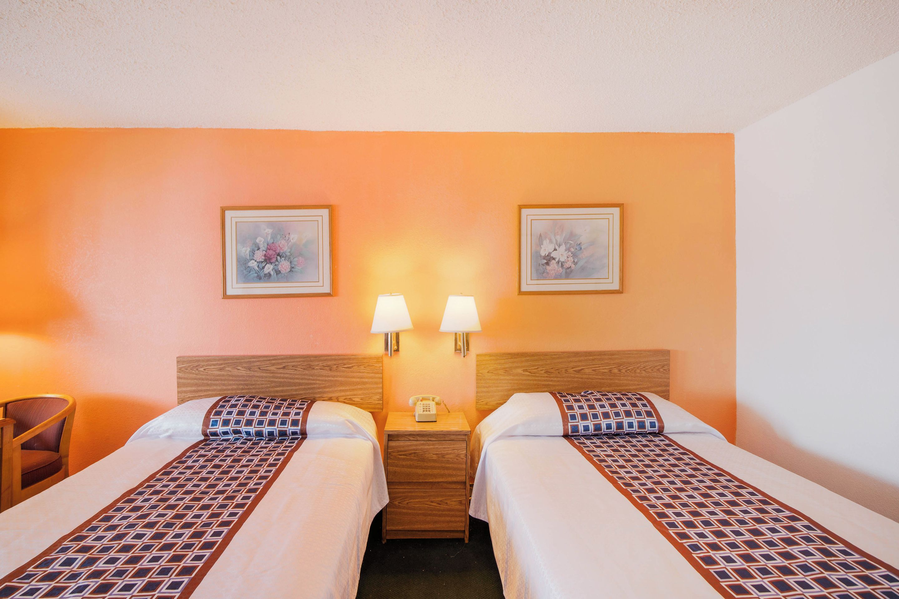 A hotel room with two beds, a nightstand with a lamp, and two framed pictures on the wall.