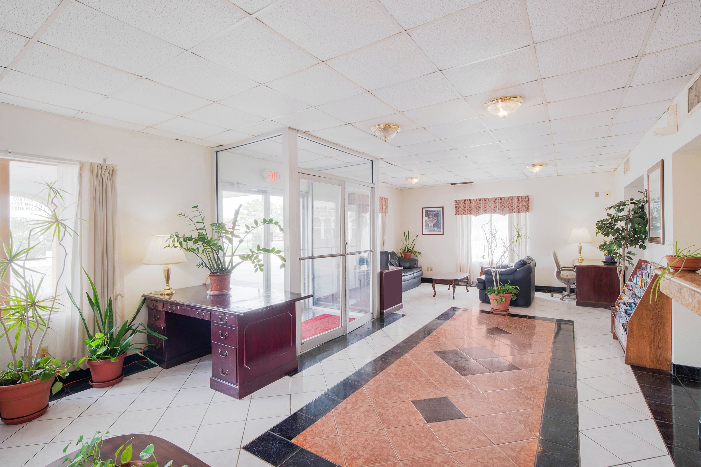 A hotel lobby with a reception desk, seating area, and potted plants.