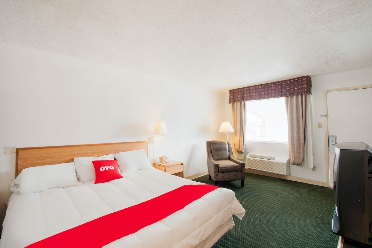 Una habitación de hotel con cama, una silla, televisión y ventana con cortinas.