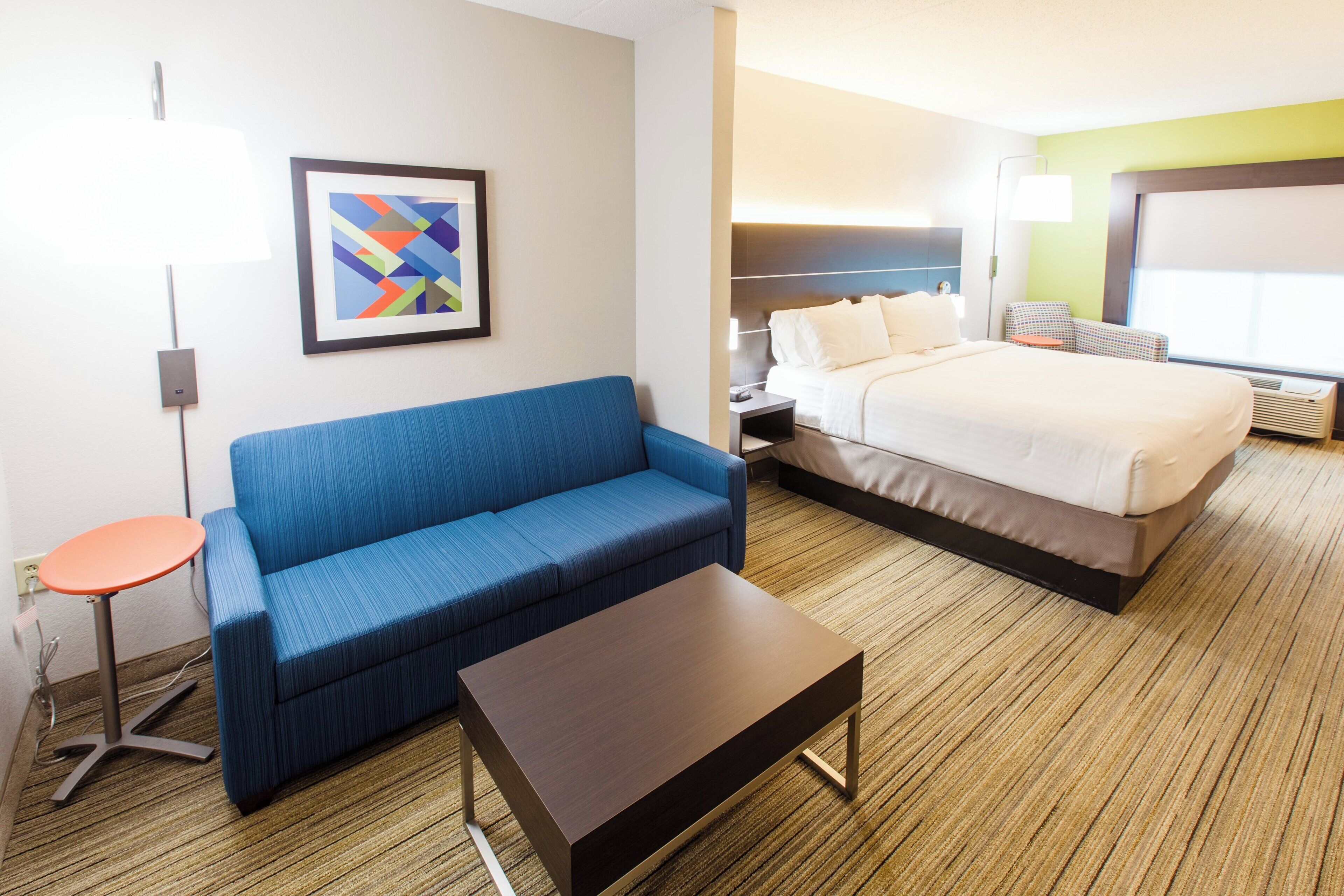 Ein Hotelzimmer mit einem Bett, einem blauen Sofa, einem kleinen Tisch, einem gerahmten Bild an der Wand und einer Lampe.