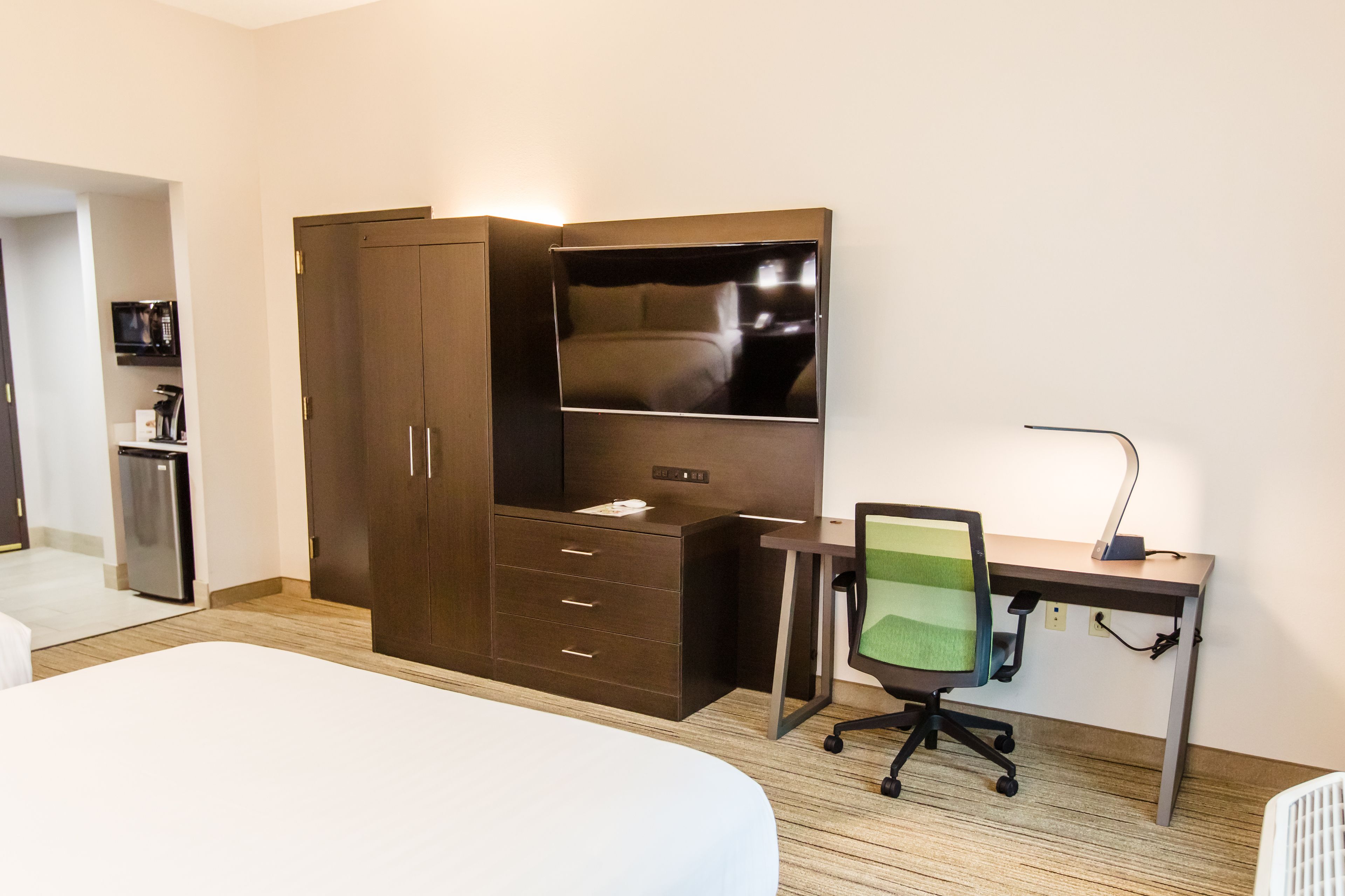 Una habitación de hotel con cama, escritorio, silla, armario y microondas.