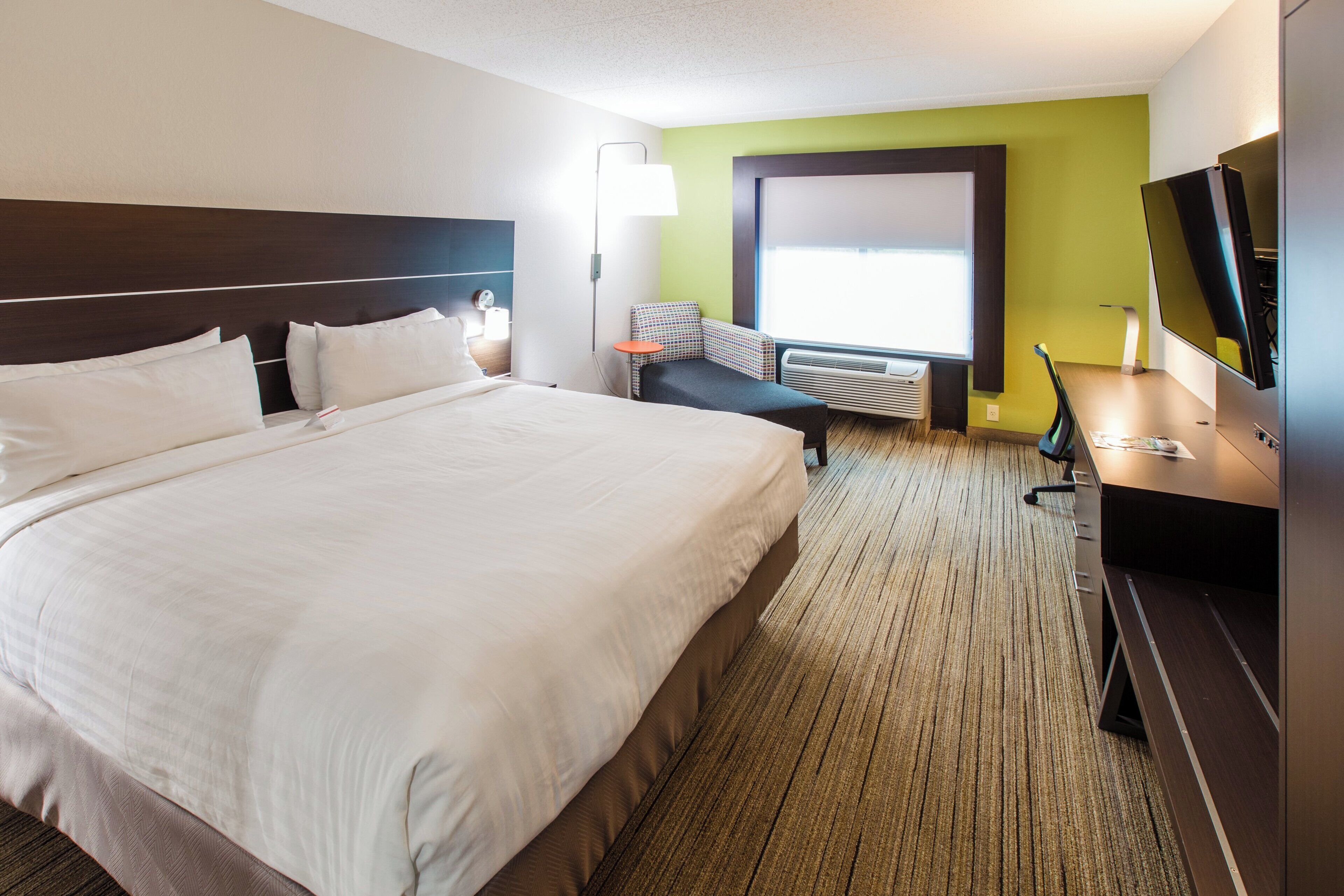 Habitación de hotel con una cama grande, un escritorio con ordenador, un televisor y una ventana con persianas.