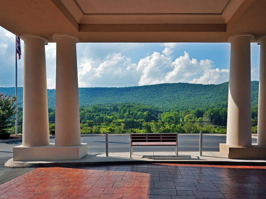 A covered outdoor area with a bench and a view of a forested hill.