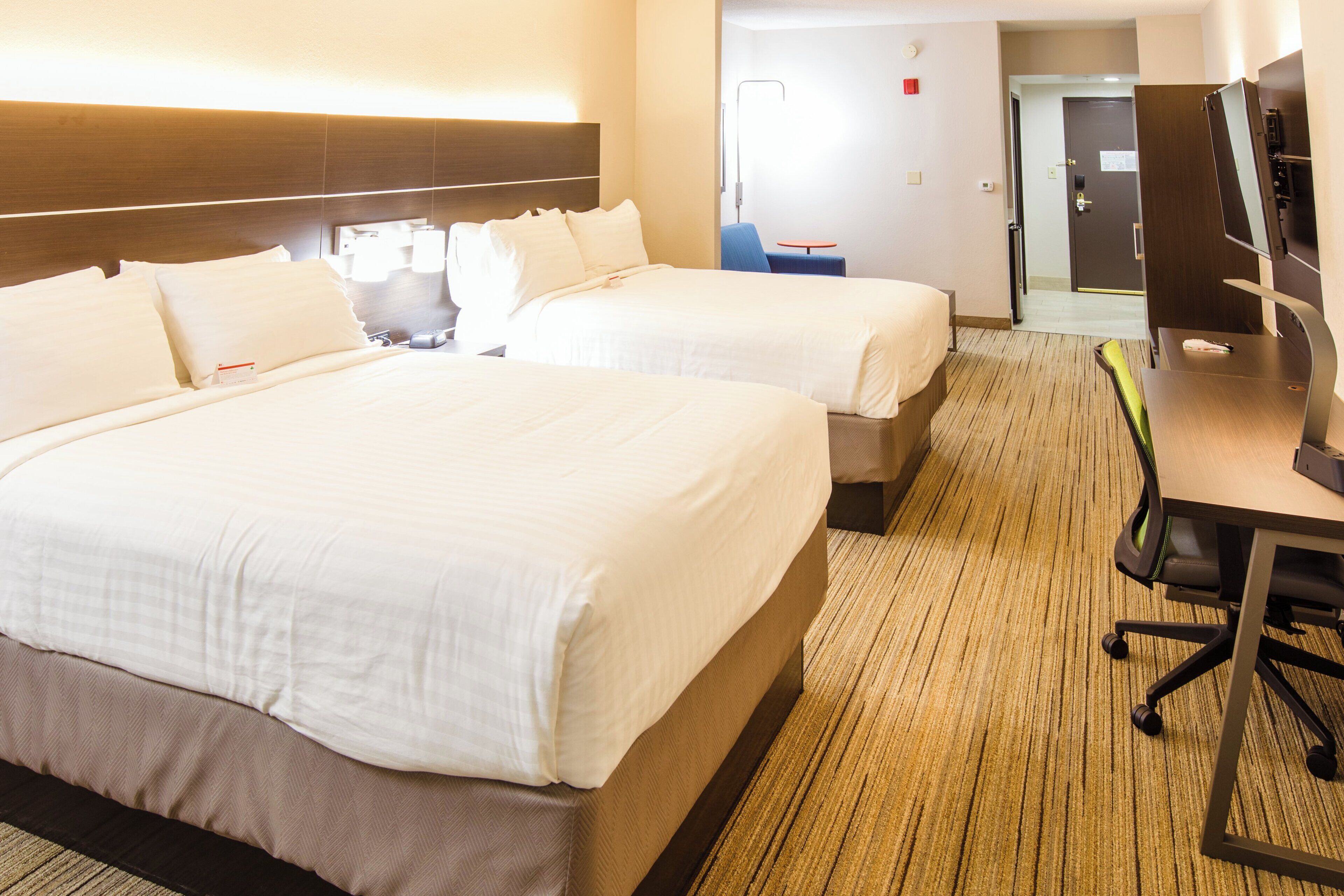 Quarto de hotel com duas camas, uma escrivaninha, uma cadeira e uma televisão.