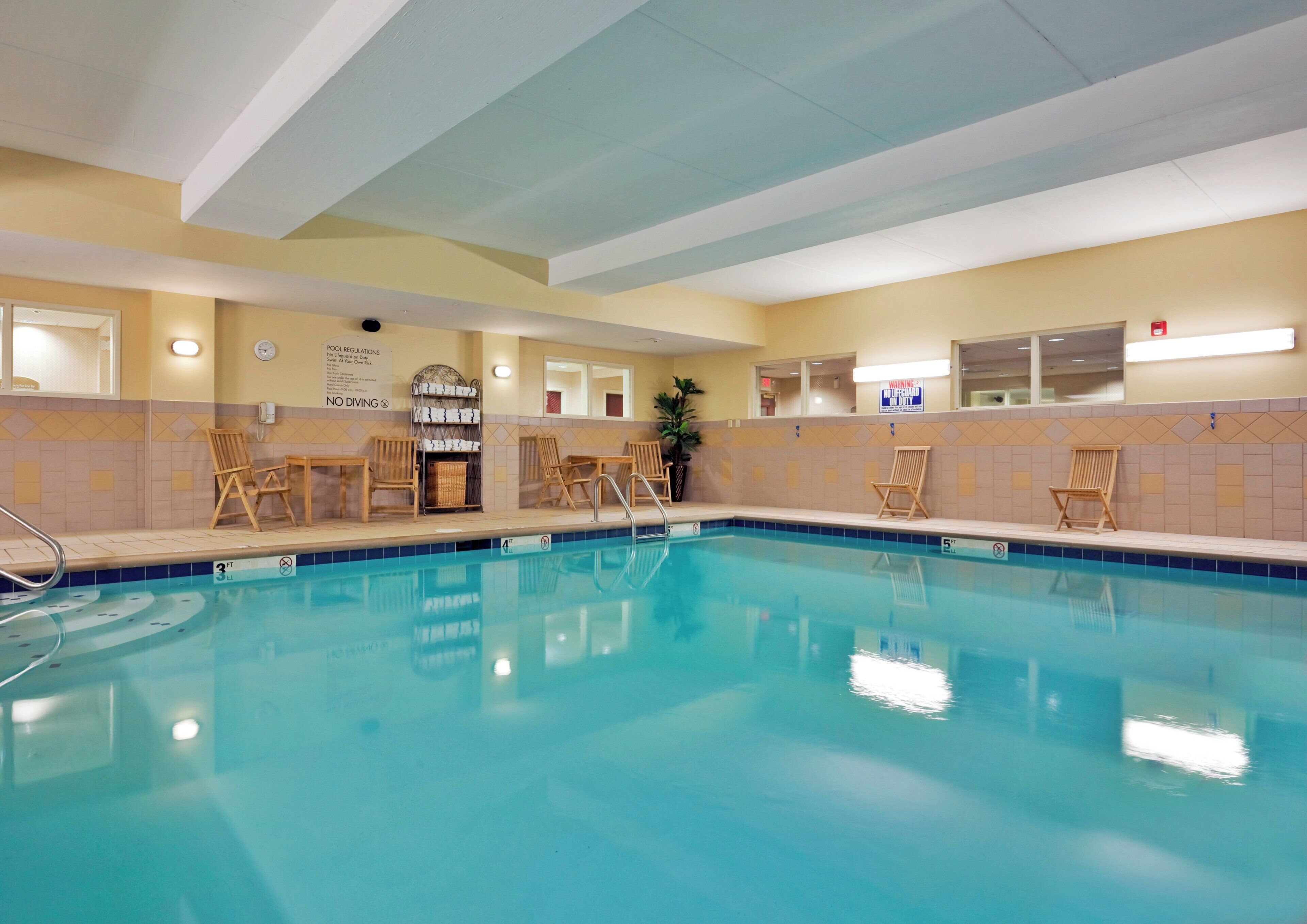 Una piscina interior con agua cristalina, sillones de madera para relajarse y una zona junto a la piscina con un cartel que indica que no se permite bucear.
