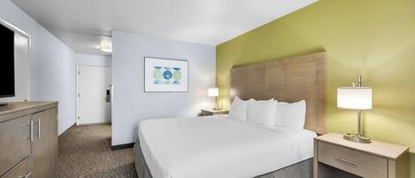 A hotel room with a large bed, a bedside table with a lamp, a dresser, and a framed picture on the wall.