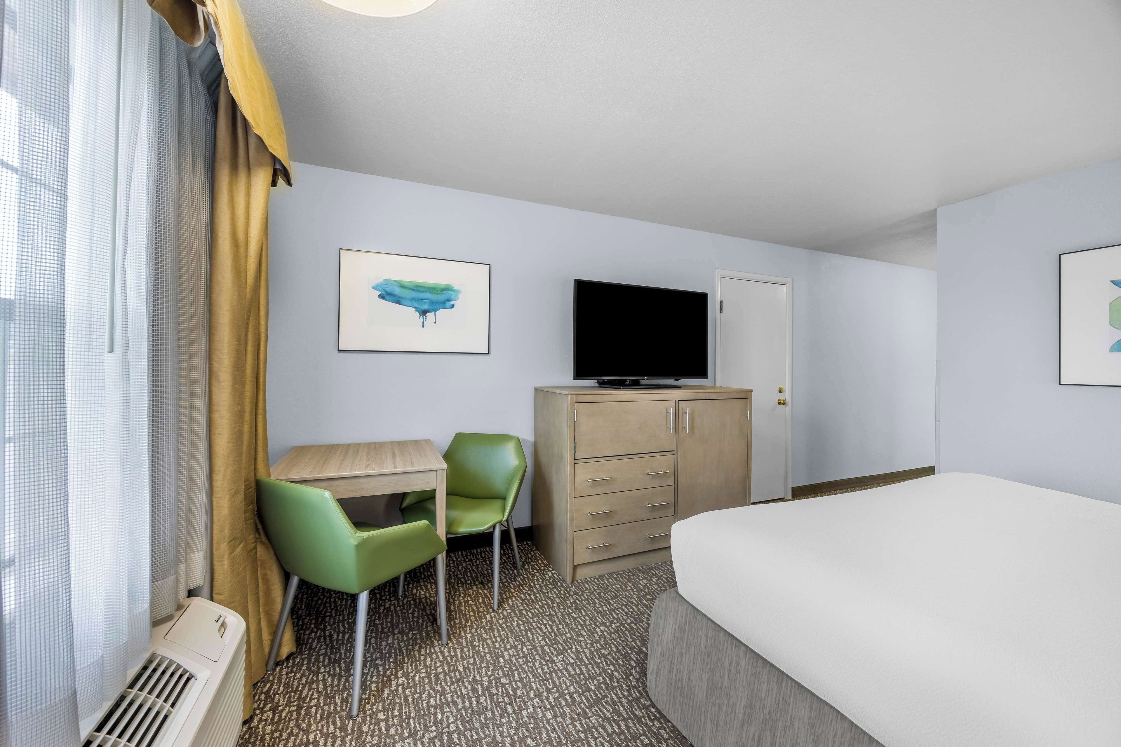 A hotel room with a bed, a desk with a chair, a television on a cabinet, and artwork on the walls.