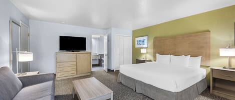 A hotel room with a large bed, a sofa, a desk, a television, and a bathroom visible through an open door.