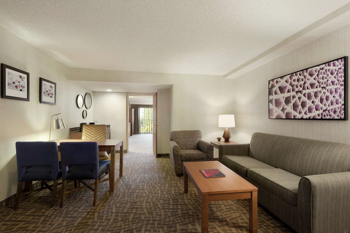 A hotel room with a sofa, two armchairs, a small table, a lamp, and a large abstract painting on the wall.