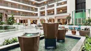Un lobby de hotel con varios niveles, una fuente central, zonas de estar y balcones.