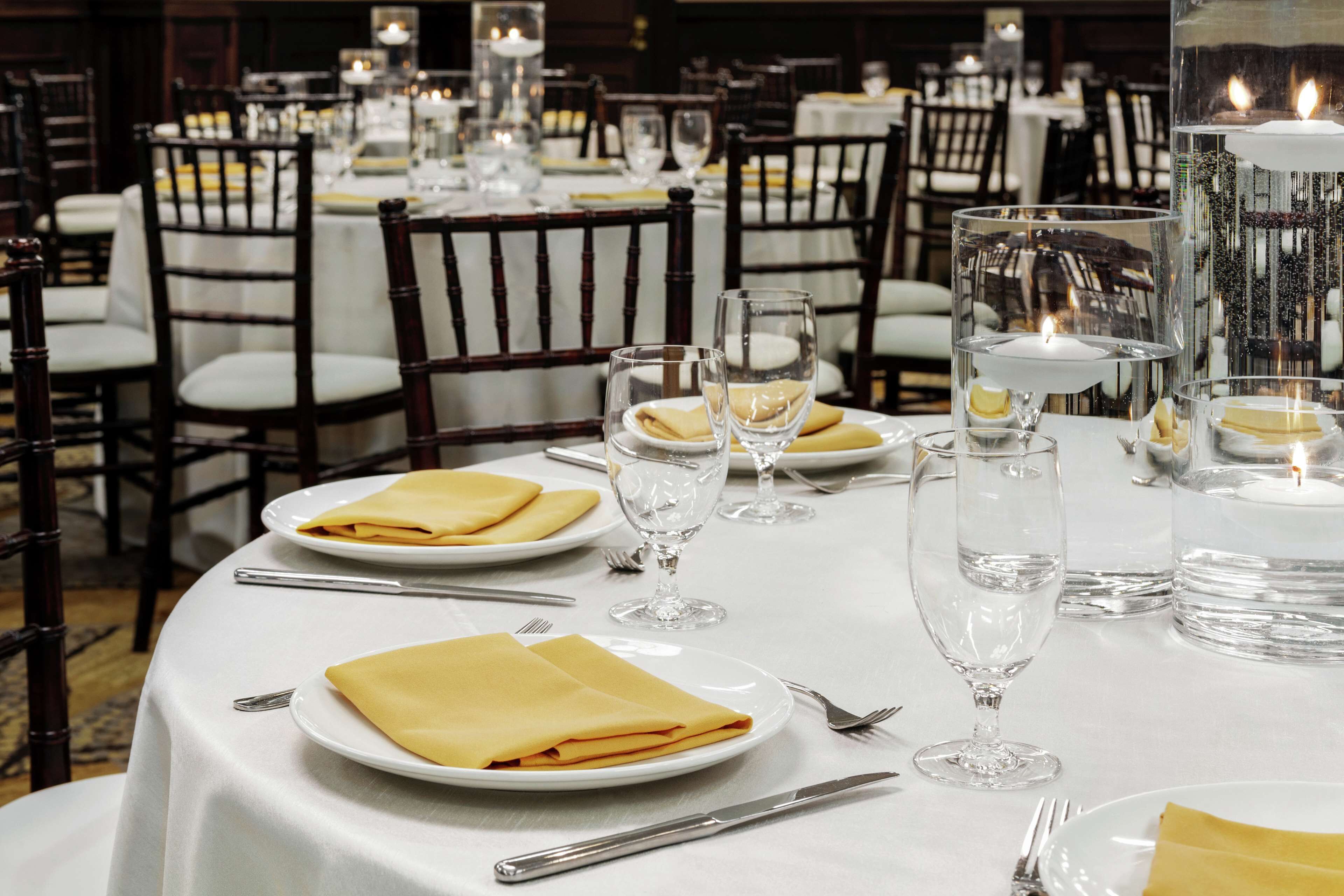 A dining area with round tables set for a meal, complete with plates, napkins, cutlery, and candles.