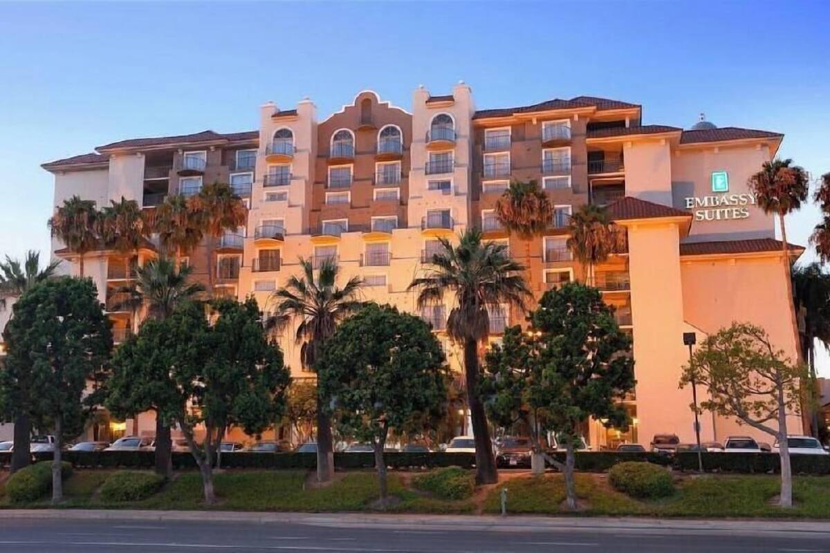 A multi-story hotel with balconies, palm trees, and a clear sky.