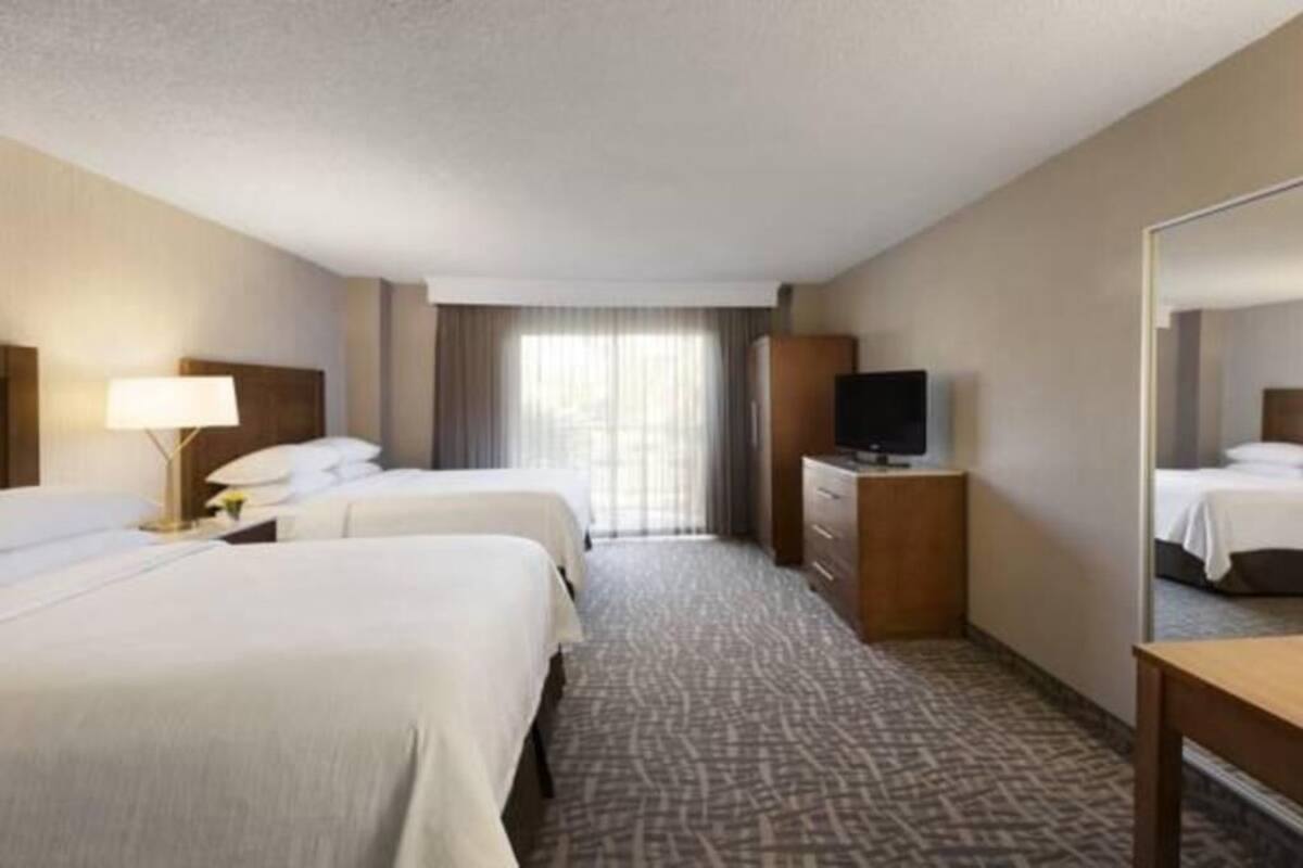 A hotel room with two beds, a desk, a television, and a mirror.