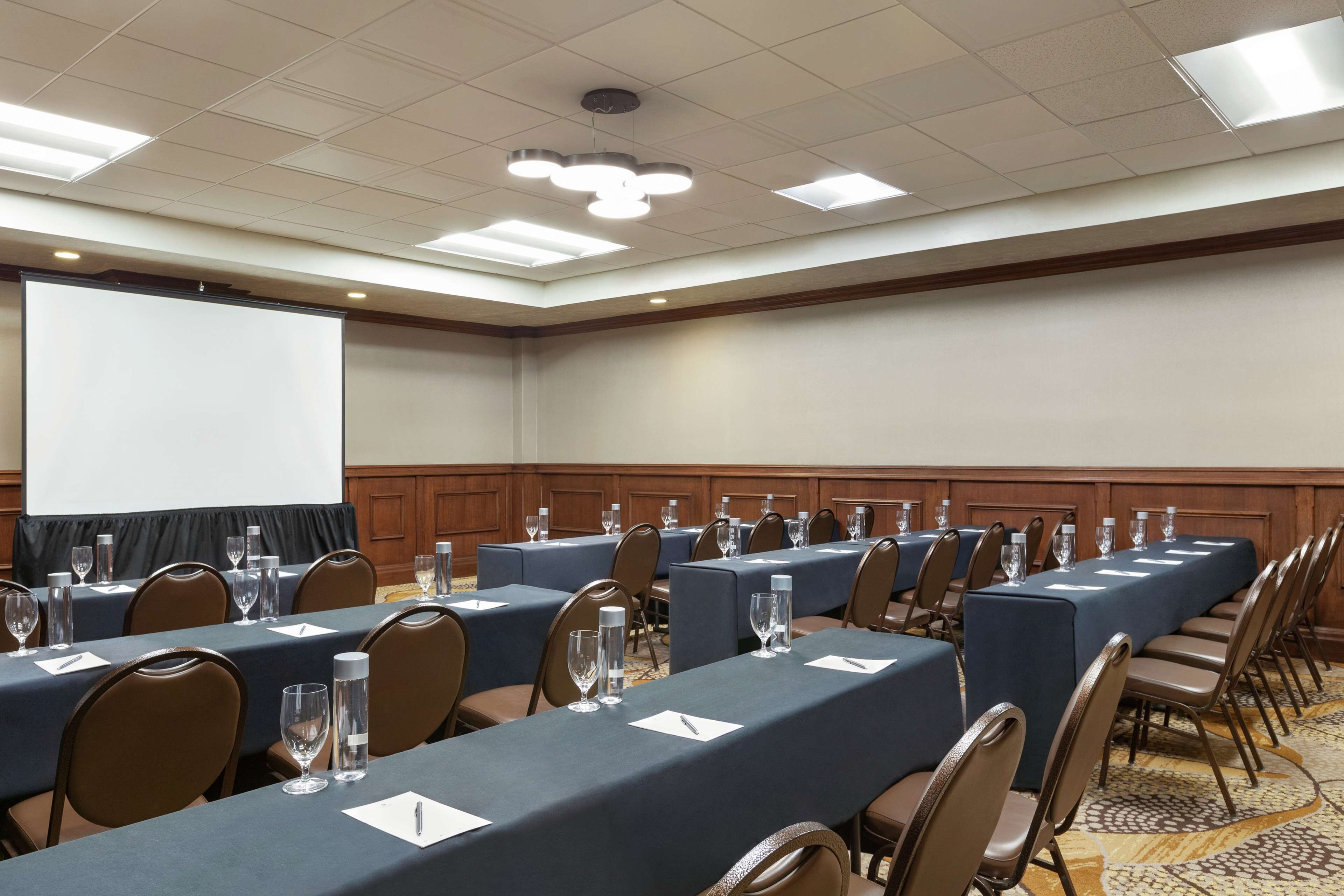 A conference room with long tables, chairs, and a projection screen.