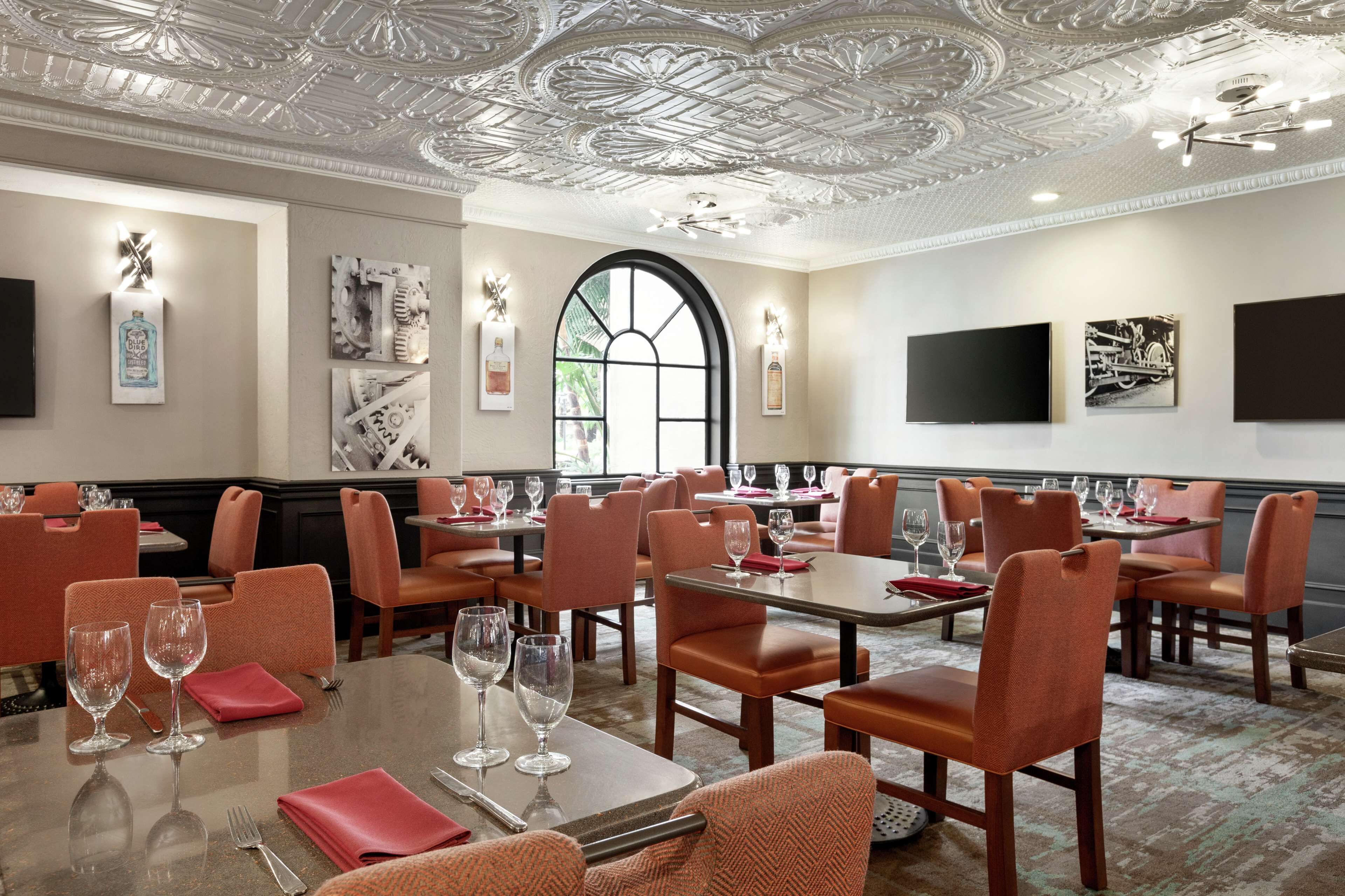 A dining area with tables and chairs, a large arched window, and wall-mounted artwork.