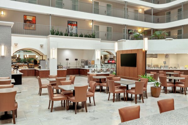 A spacious indoor area with multiple dining tables and chairs, a kitchen area in the background, and a second-floor balcony with railings.