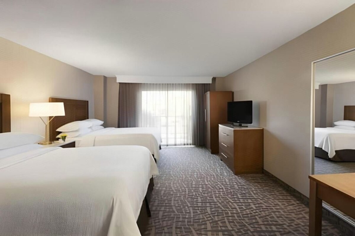 Habitación de hotel con dos camas, un televisor, un aparador y un espejo grande.