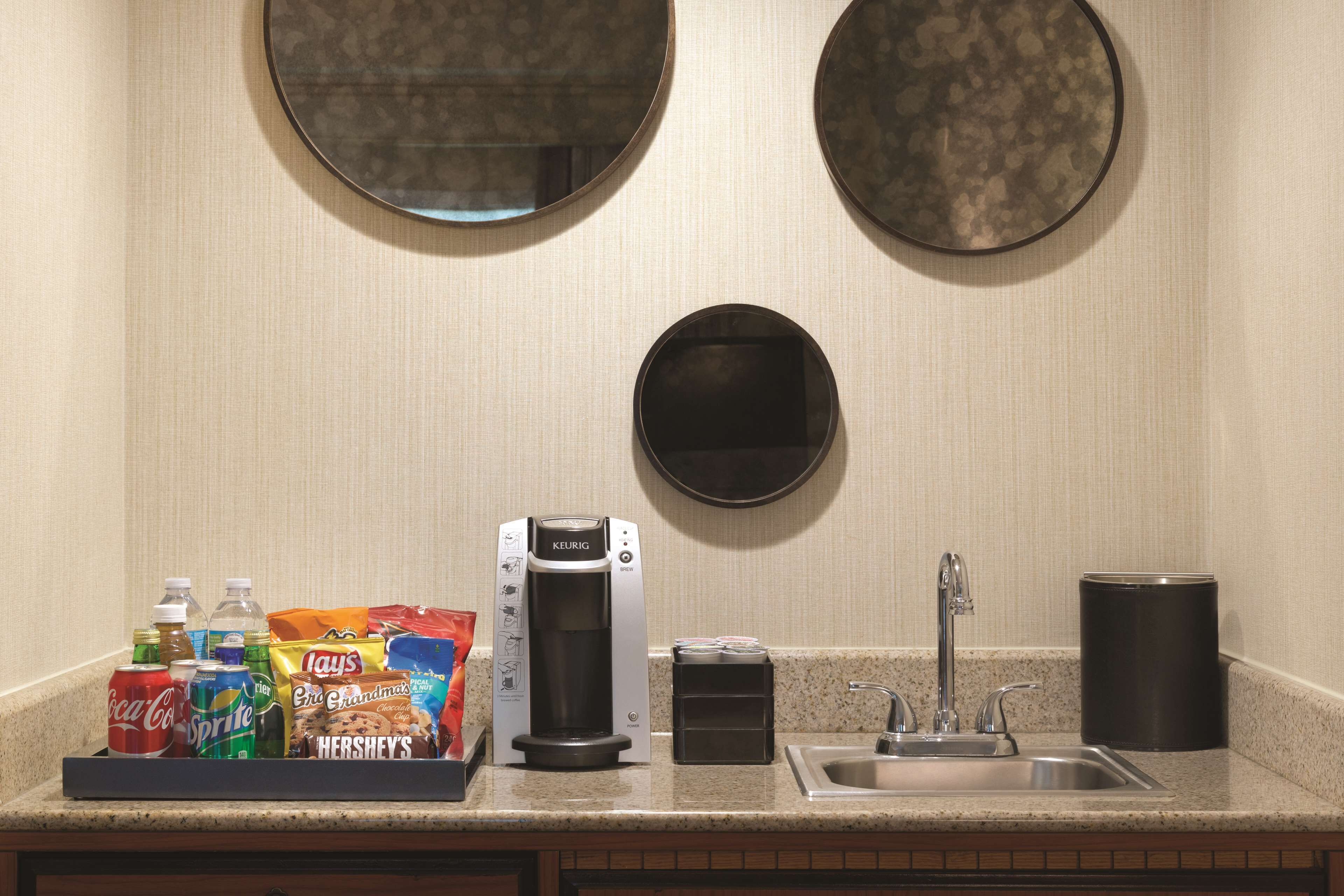 A kitchenette with a coffee maker, a sink, and a tray of snacks.